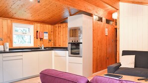 A compact kitchen with a microwave, oven, and sink. There is a purple sofa and a small table with a remote control and a book. - 2 bedroom accommodation in Charlcot, near Masham (Charlcot, near Masham)
