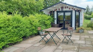 A patio with a wooden table and chairs, surrounded by stone tiles and lush greenery. - 2 bedroom accommodation in Toynton-All-Saints, near Spilsby (Toynton-All-Saints, near Spilsby)