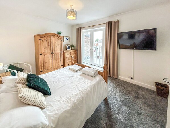 Un dormitorio con cama, armario de madera, televisión y ventana con cortinas.