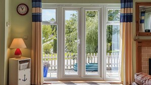 Ein Zimmer mit einer Schiebetür zum Balkon, einer roten Lampe, einem weißen Schrank mit Anker-Motiv und einem braunen Ledersofa.