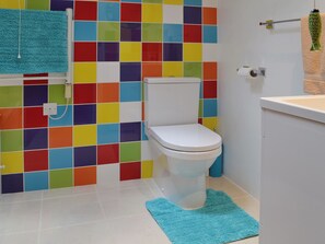 Une salle de bain avec des toilettes blanches, des murs recouverts de carreaux colorés, un tapis bleu et un porte-serviettes avec une serviette.