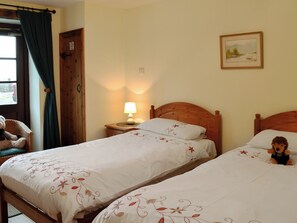 Une chambre d’hôtel avec deux lits, une tête de lit en bois, une table de chevet avec une lampe, une chaise en osier et une porte avec une pancarte.