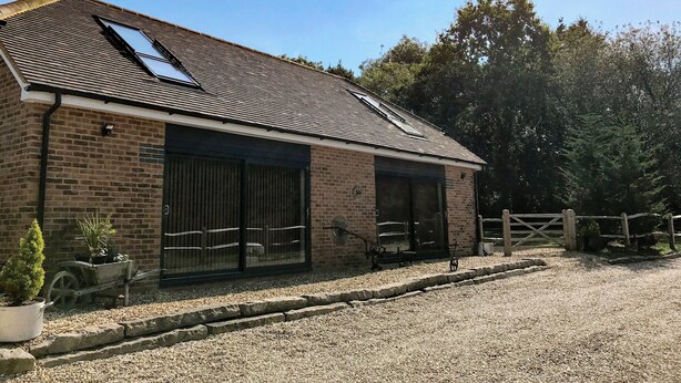 A brick building with a sloped roof, large windows, and a gravel driveway. - 3 bedroom accommodation in Farnham (Farnham)