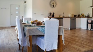 A dining area with a table set for four, a clock on the wall, and a kitchen in the background. - 3 bedroom accommodation in Farnham (Farnham)