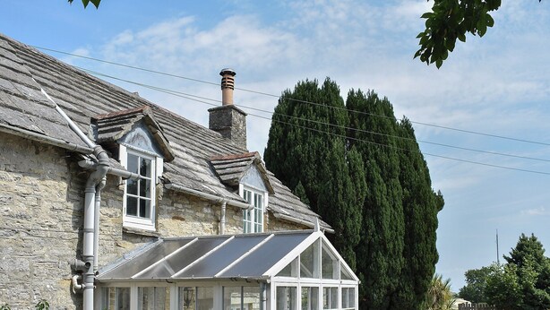 A stone house with a conservatory, a chimney, and a large tree in the background. - 3 bedroom accommodation in Harmans Cross, near Swanage (Harmans Cross, near Swanage)