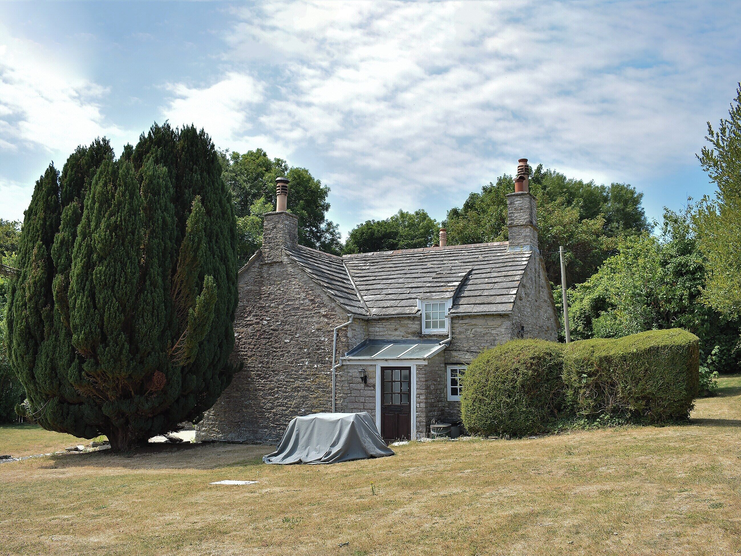 A stone house with a sloped roof, a chimney, and a covered outdoor area.