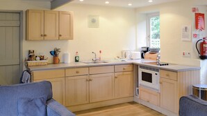 A compact kitchen with wooden cabinets, a microwave, and a sink. There are two blue chairs in the room. - 2 bedroom accommodation in St Kew, near Port Isaac (St Kew, near Port Isaac)