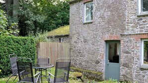 A stone building with a small door and window, surrounded by a garden with chairs and a table. - 2 bedroom accommodation in St Kew, near Port Isaac (St Kew, near Port Isaac)