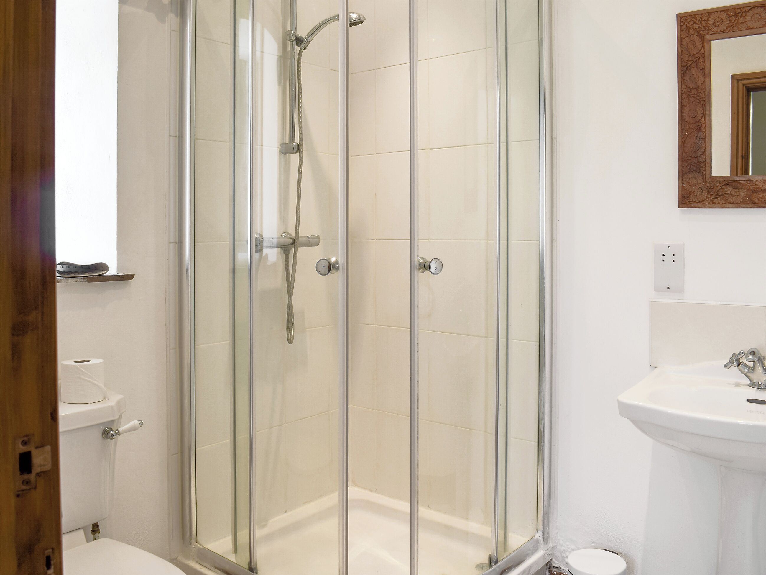 A glass-enclosed shower with a handheld showerhead and a wall-mounted faucet.