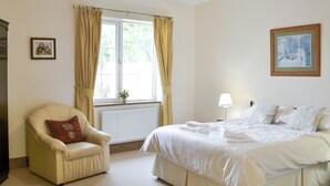Een slaapkamer met een bed, een stoel, een radiator, een raam met gordijnen en een lamp.