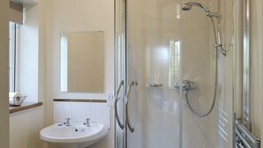 Een badkamer met een douchecabine van glas, een witte wastafel en een spiegel.