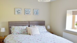 Quarto com cama, colcha florida, abajures e três quadros florais pendurados na parede.