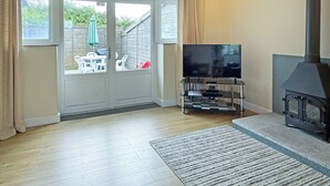 Ein Wohnzimmer mit Fernseher, Kamin und Blick durch eine Glastür auf einen Außenbereich mit Stühlen und einem Tisch.