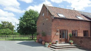 A brick building with a sloped roof, a wooden door, and a small porch with potted plants.