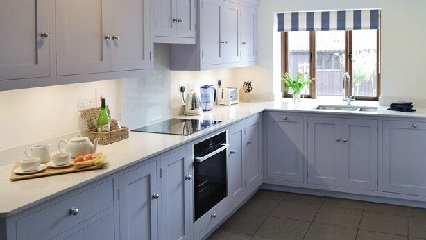 A modern kitchen with grey cabinets, a built-in dishwasher, and a window with a striped valance.