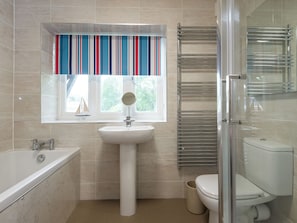 A bathroom with a bathtub, sink, toilet, and a window with a striped curtain.