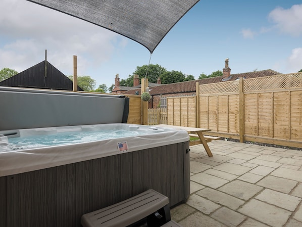 A hot tub with a wooden bench, a wooden fence, and a clear sky.