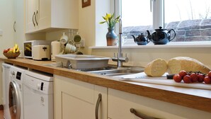 A kitchen with a washing machine, a sink, a window with a view, and various kitchen items on the counter. - 2 bedroom accommodation in Aspatria (Aspatria)