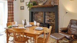A dining area with a wooden table set for four, surrounded by wooden chairs. A fireplace with a stone facade is visible in the background. - 2 bedroom accommodation in Aspatria (Aspatria)
