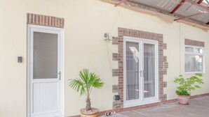 Un bâtiment doté d’un patio couvert, comprenant une porte, une fenêtre et deux plantes en pot.