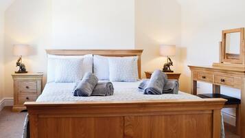 A neatly made bed with pillows and rolled towels, a wooden nightstand with a lamp, and a dresser with a mirror.