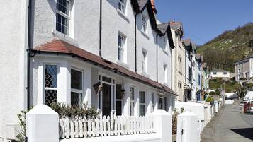 A row of white buildings with a white picket fence, a clear sky, and a hilly background.