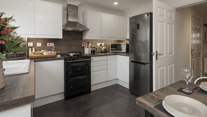 Una cocina moderna con armarios blancos, un refrigerador de acero inoxidable, un horno empotrado y un microondas.