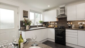 Una cocina moderna con armarios blancos, una estufa negra y un comedor con una mesa lista para dos.