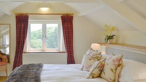 Een slaapkamer met een bed, een raam met gordijnen, een bedlampje en een plant op een plank.