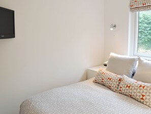 A bedroom with a bed, a nightstand, a television, and a window with a view of greenery. - 2 bedroom accommodation in Lelant, near St Ives (Lelant, near St Ives)