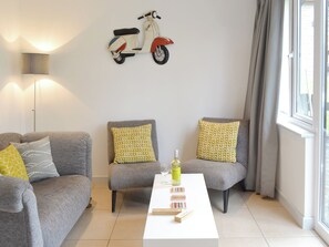 Ett modernt vardagsrum med en soffa, två fåtöljer, ett soffbord med böcker och en flaska samt en sparkcykel som hänger på väggen.