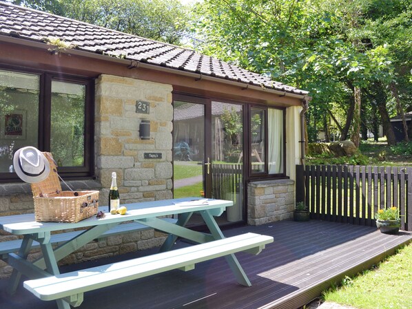 A stone building with a tiled roof, a picnic table with a basket and a bottle, and a wooden fence.