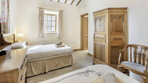 A bedroom with two beds, a wooden wardrobe, a chair, a desk, and a window with curtains.