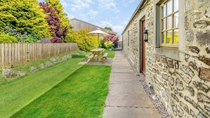 A stone building with a stone pathway leading to a wooden picnic table with an umbrella.
