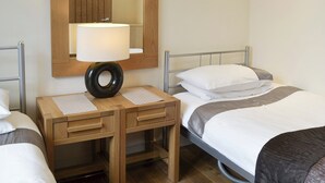 Une chambre d’hôtel avec un lit, une table de chevet avec une lampe, un miroir et une petite table en bois.