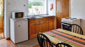 Eine kleine Küche mit weißen Geräten, Holzschränken, einem Fenster mit Blick und einem Essbereich mit gestreiftem Tischlein.