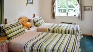 Ein Schlafzimmer mit zwei Betten, gestreifter Bettwäsche, einem Holzkopfteil, einem Nachttisch mit Lampe und einem Fenster mit Vorhängen.