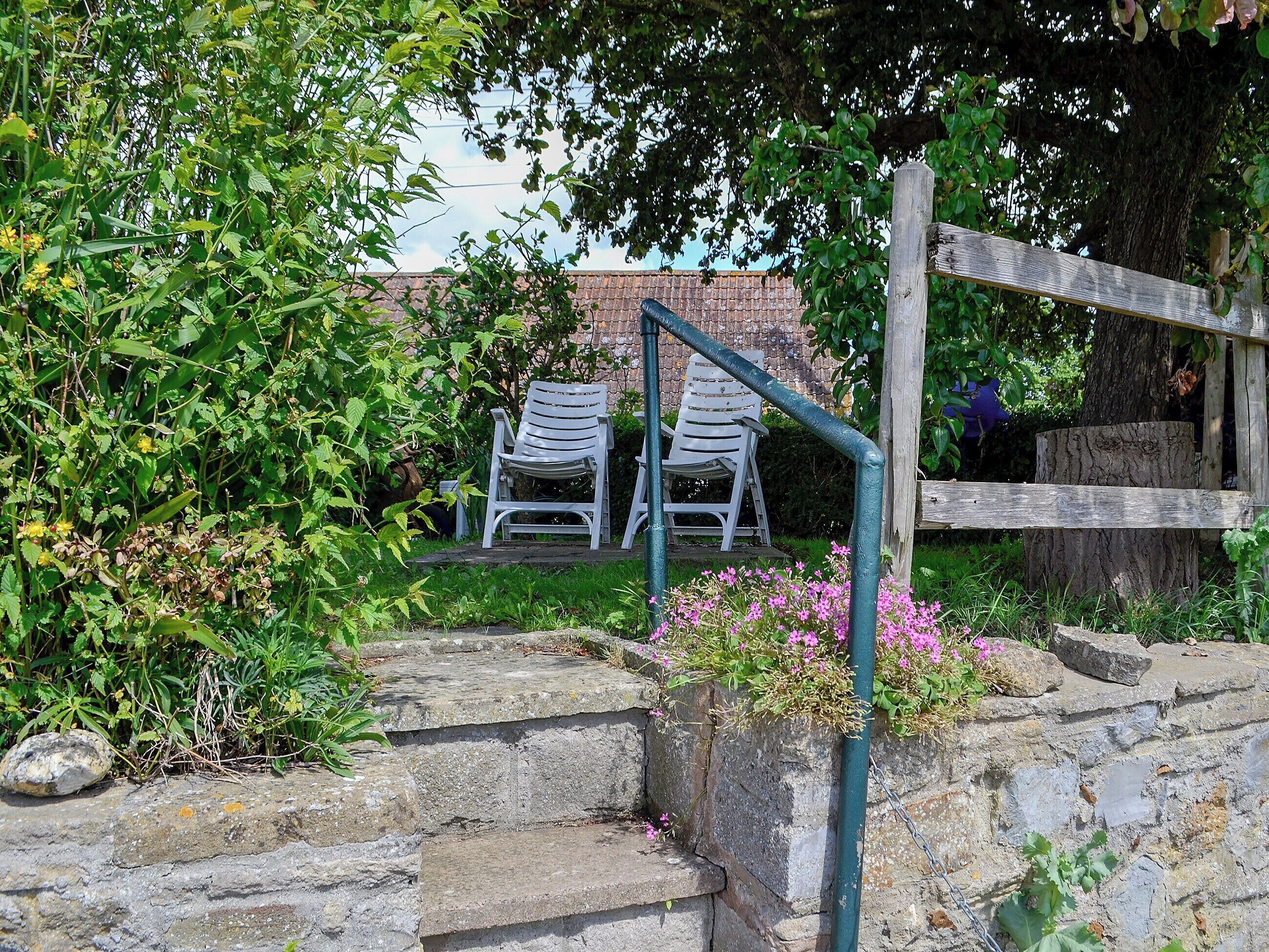 Een tuin met stenen traptreden naar een zitgedeelte met twee witte stoelen.