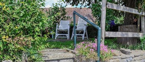 Een tuin met stenen traptreden naar een zitgedeelte met twee witte stoelen.