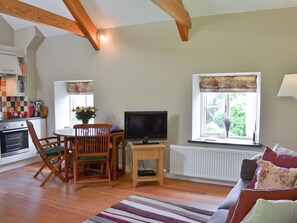 A living room with a television, a dining table with chairs, a sofa, and a window with a view of greenery.