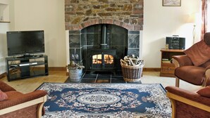 A living room with a stone fireplace, a television, and two armchairs. - 2 bedroom accommodation in Northlew, near Tavistock (Northlew, near Tavistock)