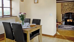 A dining area with a wooden table, black chairs, a vase with flowers, a clock, and a fireplace in the background. - 2 bedroom accommodation in Northlew, near Tavistock (Northlew, near Tavistock)