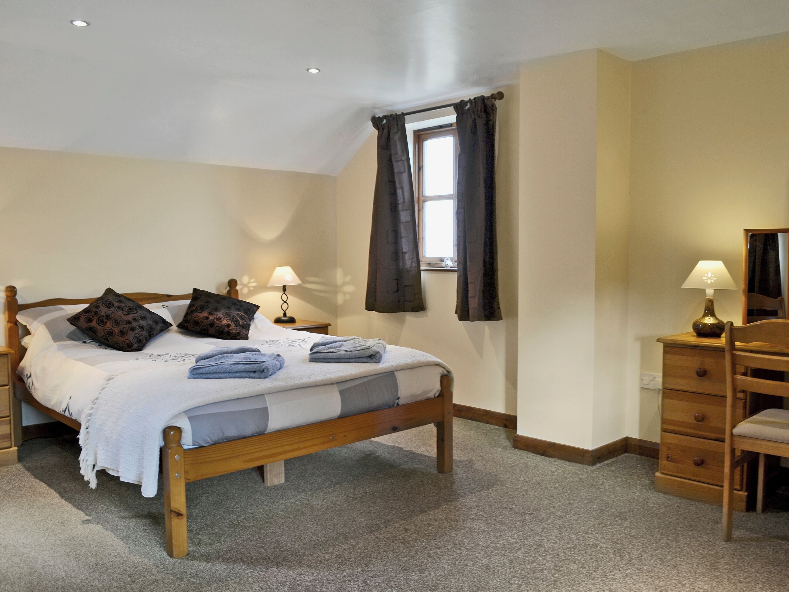 Une chambre à coucher avec un lit en bois, une table de chevet avec une lampe, une commode et une fenêtre avec des rideaux.