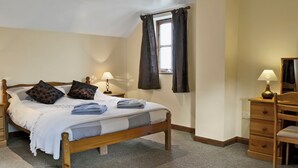A bedroom with a wooden bed, a nightstand with a lamp, a dresser, and a window with curtains. - 2 bedroom accommodation in Northlew, near Tavistock (Northlew, near Tavistock)