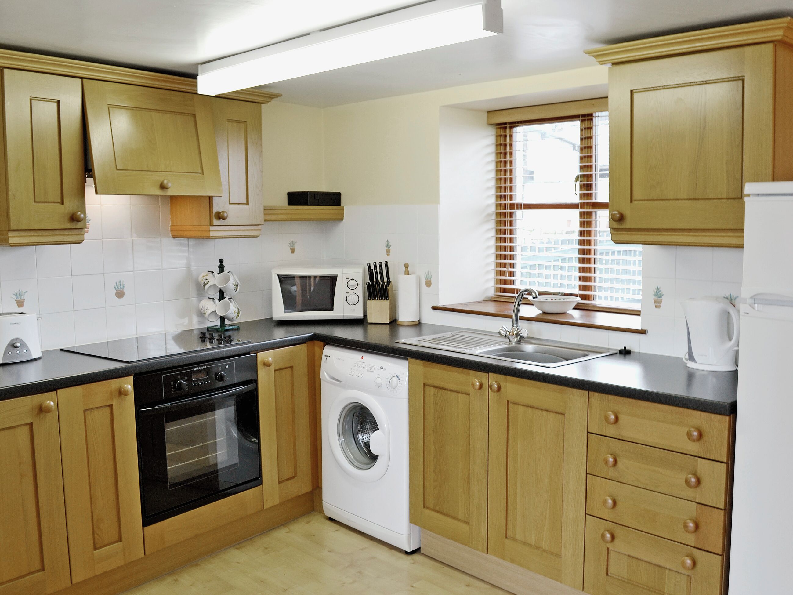 A kitchen with wooden cabinets, a microwave, a washing machine, and a sink.