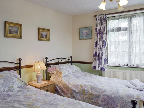 A bedroom with two single beds, a bedside table with a lamp, and a window with floral curtains.