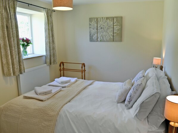 A neatly made bed with white linens and a quilt, a bedside lamp, and a wall-mounted artwork. - Acorn Cottage - UKC1812 (North Perrott, near Crewkerne)