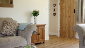 A living room with a sofa, a wooden cabinet, a glass bowl with green plants, and a door with a wooden panel. - Acorn Cottage - UKC1812 (North Perrott, near Crewkerne)