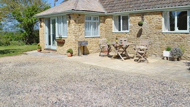 A stone house with a tiled roof, a gravel driveway, and a wooden table with chairs outside. - Acorn Cottage - UKC1812 (North Perrott, near Crewkerne)