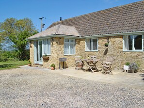 A stone house with a tiled roof, a gravel driveway, and a wooden table with chairs outside. - Acorn Cottage - UKC1812 (North Perrott, near Crewkerne)